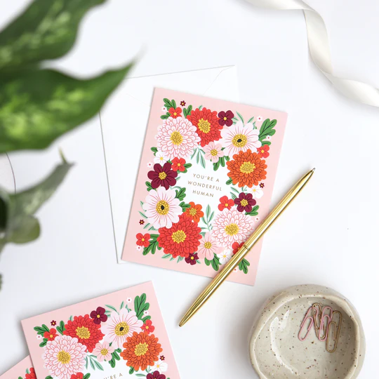You're a Wonderful Human greeting card in a beautiful arrangement of warm toned florals among a small bowl of clips, gold pen and green plant